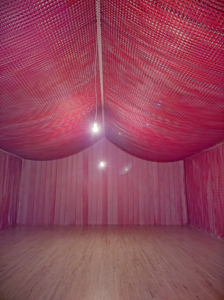 War Room installation (2015/2022) by Cornelia Parker. Tent-like installation is decorated by rows of red textiles with poppy-shaped holes in them, which are the off-cuts from the process of manufacturing red poppy pins worn for the Remembrance Day in the UK.