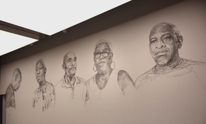 Five portraits of three men and two women drawn on a wall.